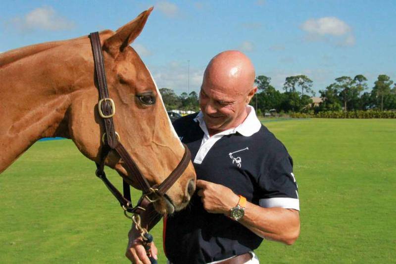 A man playing polo on a brown horse in a lush green field.